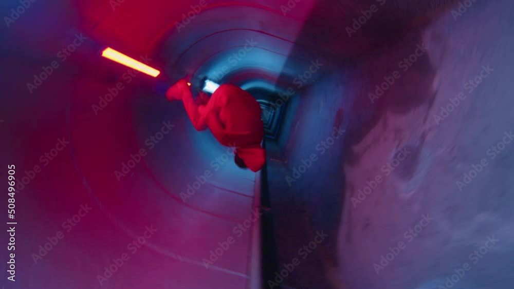 Camera roll of parkour athlete running through dark underground tunnel with neon light and performing side flip