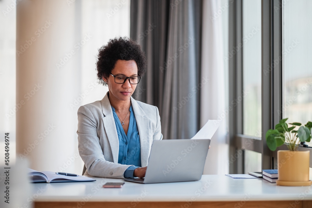 Businesswoman with papers working on laptop while sitting at office desk Businesswoman with papers working on laptop while sitting at office desk