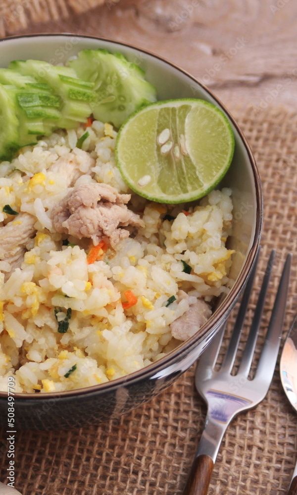 Pork Fried Rice, Chinese Style Fried Rice in a Bowl with Cucumber and Lemon Served on a brown wooden table. Pork Fried Rice, Chinese Style Fried Rice in a Bowl with Cucumber and Lemon Served on a brown wooden table.
