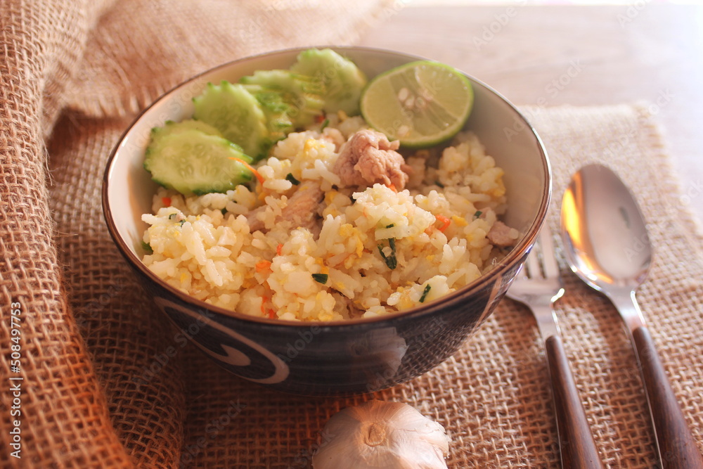 Pork Fried Rice, Chinese Style Fried Rice in a Bowl with Cucumber and Lemon Served on a brown wooden table. Pork Fried Rice, Chinese Style Fried Rice in a Bowl with Cucumber and Lemon Served on a brown wooden table.