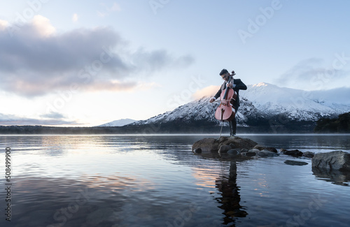 Musician playing cello by the lake with snow capped mountains on the back