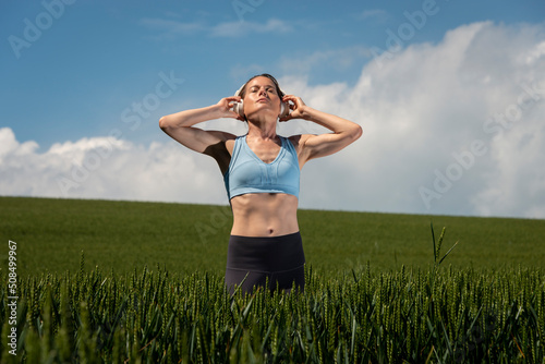 Sporty, fit woman standing in a green field wearing a pair of headphones listening to music, getting away from it all.