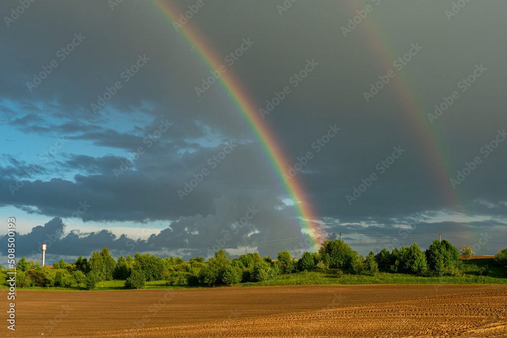A multicolored rainbow over a plowed agricultural field during the rain. Beautiful spring natural landscape. Beautiful nature of Belarus. A multicolored rainbow over a plowed agricultural field during the rain. Beautiful spring natural landscape. Beautiful nature of Belarus.