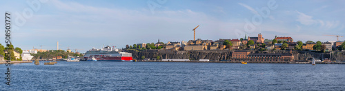 Panorama view over the bay Stockholms Ström in evening light with the district Södermalm and cruise ships and island with a castle and brick building a sunny evening in Stockholm