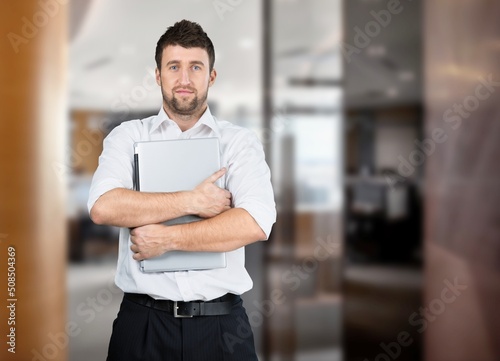 Young man standing holding laptop on office background
