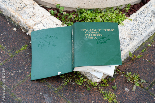 A thick book in hardcover lies on the street, thrown away on the cover is written in Russian - Phraseological Dictionary of the Russian Language. photo