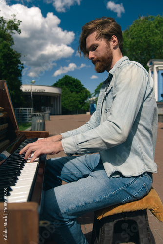 Obraz na płótnie Street musician playing old piano in downtown. Young bearded man pianist playing music outdoors. Handsome talented busker. w salonie