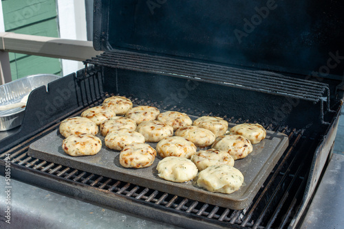 A tray of cooked round salt cod fishcakes is prepared on a barbeque. The mixture of savory, potato, salt codfish, and butter are shaped into small patties and fried in butter until golden brown.