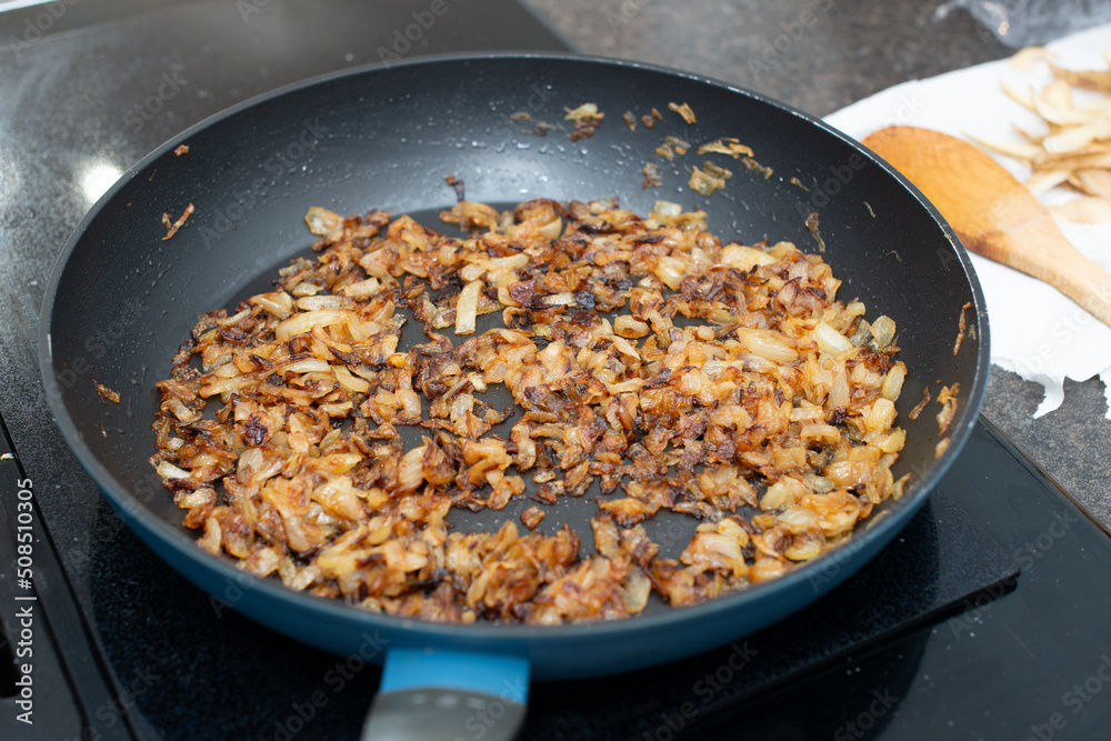 A large black colored iron frying pan full of sweet white onions minced and chopped into being fried or sauteed in butter. The edges of the diced onion have browned and caramelized to sweeten. 