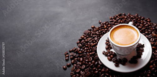 Horizontal banner with cup of coffee and coffee beans on dark stone background. Top view. Copy space.