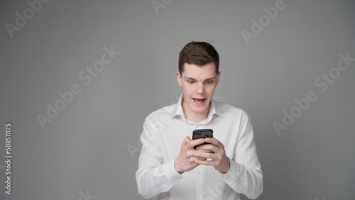 A surprised young guy looks at the screen of his smartphone. On a gray background.
