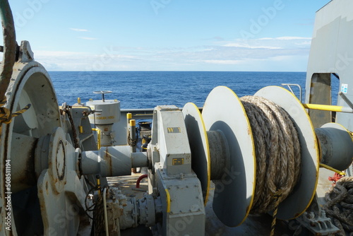 Photography Forward starboard side mooring winch and anchor windlass with heaved up white manila rope on working drum of cargo container vessel during passing Mediterranean Sea during sunny weather