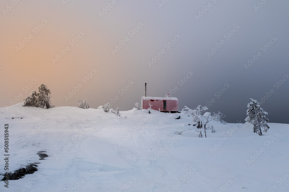 Cozy northern guest house on a snowy hill at dawn. Cabin in winter dawn.  Lonely house on a hilltop in the cool morning.
