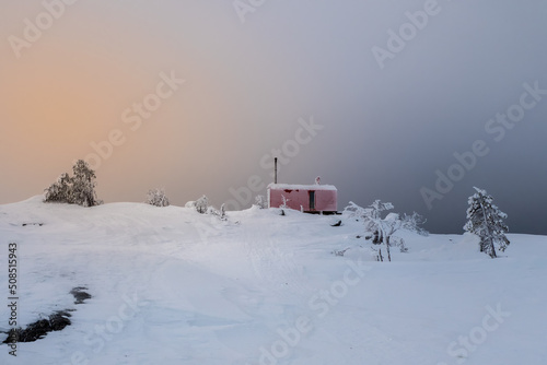 Cozy northern guest house on a snowy hill at dawn. Cabin in winter dawn. Lonely house on a hilltop in the cool morning.