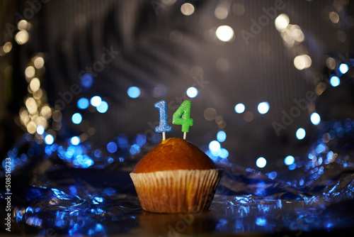 Digital gift card birthday concept. Tasty fresh homemade vanilla cupcake with number 14 fourteen on aluminium foil and blurred dark background in minimalistic style. High quality image photo