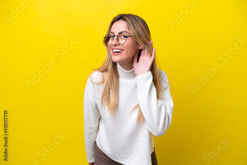 Fotografiet Young Uruguayan woman isolated on yellow background listening to something by pu