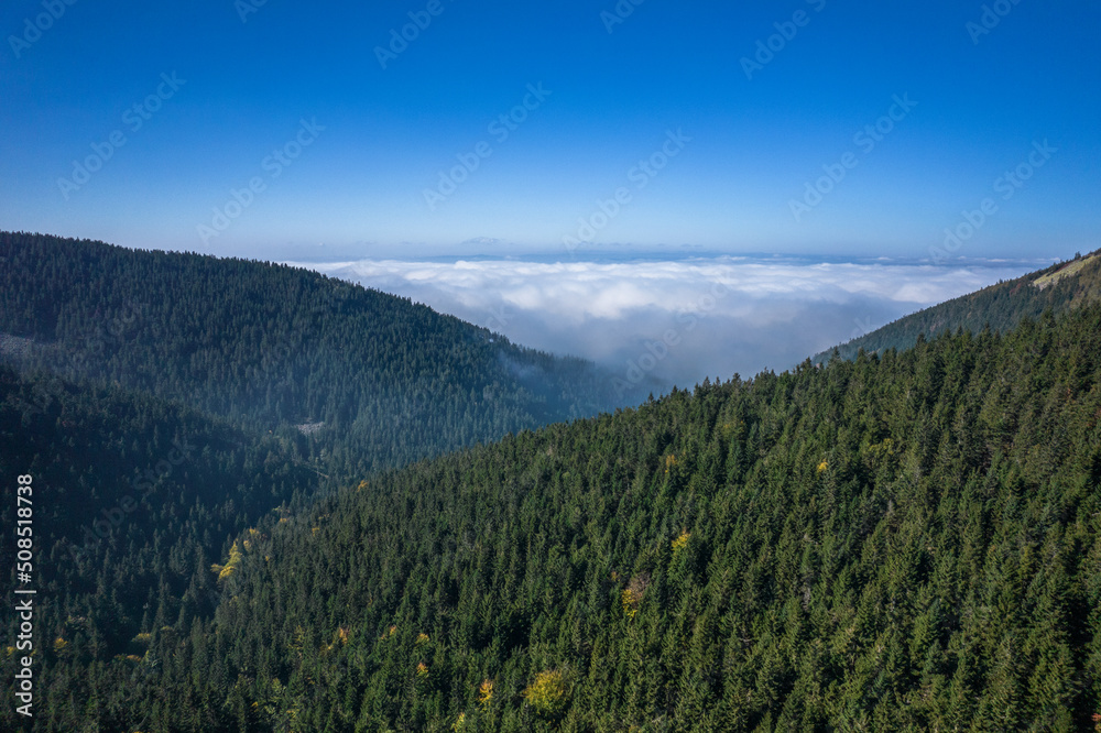 Aerial landscape of the green mountains in a daylight. Clouds low over the peaks, clear blue sky.