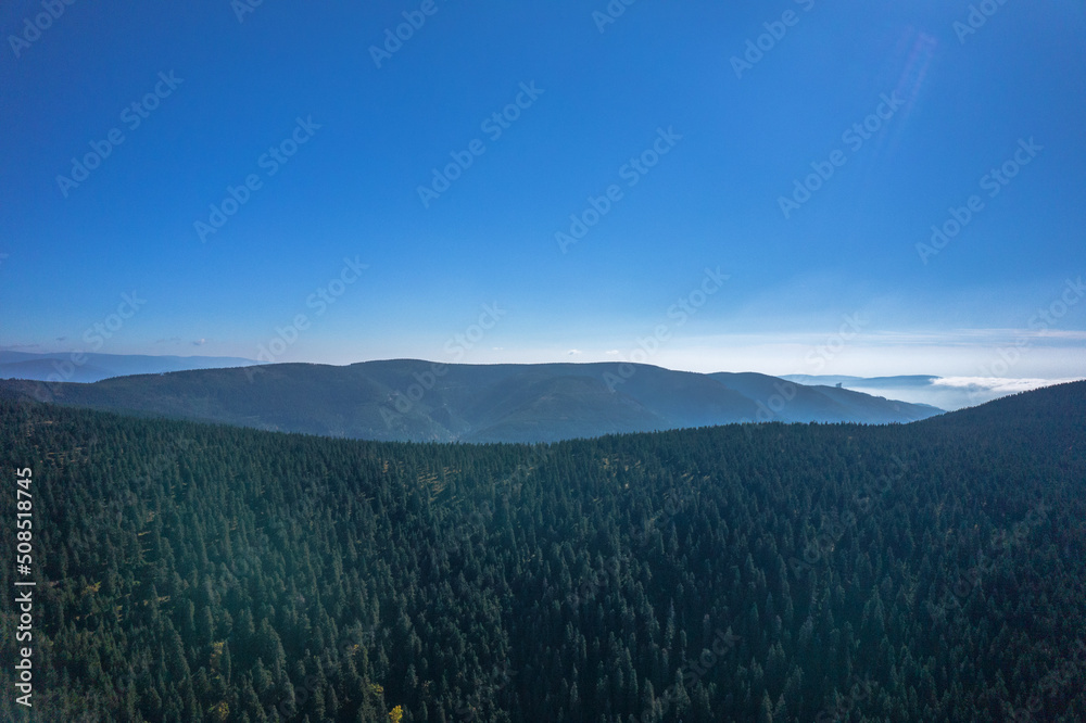 Aerial landscape of the green mountains in a daylight. Clouds low over the peaks, clear blue sky.