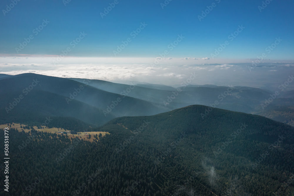 Aerial landscape of the green mountains covered with clouds. Sunny day, blue sky. 