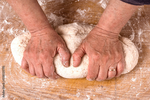 Hands kneading homemade dough for bread, pastry, and cookie. Wood rolling pin, flour. Rural food cooking. Crop view