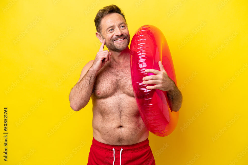 Middle age caucasian man holding inflatable donut isolated on yellow background thinking an idea while looking up