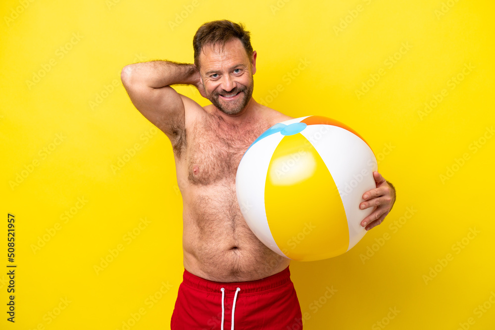Middle age caucasian man holding beach ball isolated on yellow background laughing