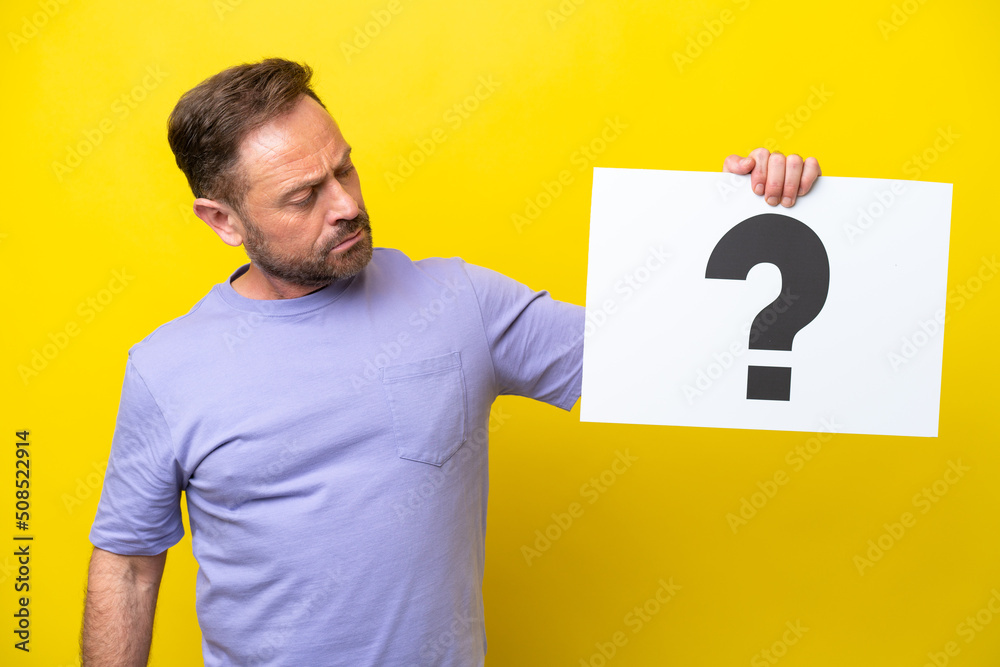 Middle age caucasian man isolated on yellow background holding a placard with question mark symbol Middle age caucasian man isolated on yellow background holding a placard with question mark symbol