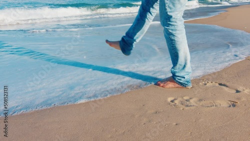 Man in blue jeans walks barefoot on the sandy beach