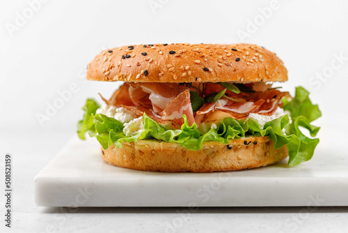Delicious burger with prosciutto, cream cheese and lettuce for breakfast, sandwich, bagel with ham, close up