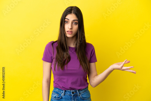 Young caucasian woman isolated on yellow background making doubts gesture