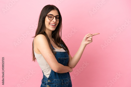 Young caucasian woman isolated on pink background pointing finger to the side