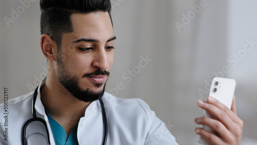 Confident qualified physician male arabian doctor use smartphone social medical app consult clients online in clinic cabinet remote communication give advice telemedicine healthcare services concept