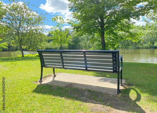 Banc de parc public en été. Lumière douce du soleil sur les arbres et le mobilier. Banc dans un parc nature près de l'eau.