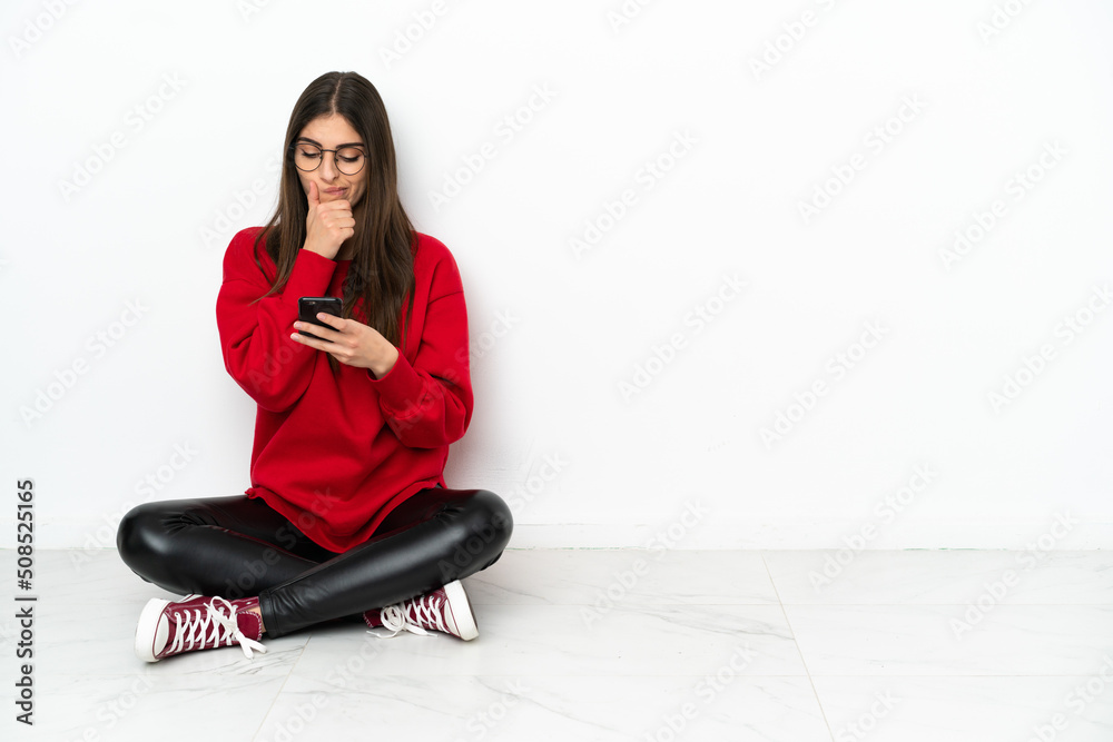 Young woman sitting on the floor isolated on white background thinking and sending a message Young woman sitting on the floor isolated on white background thinking and sending a message