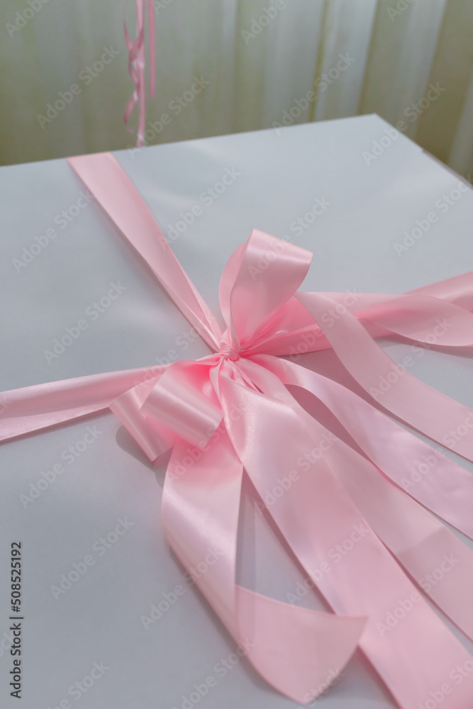 White present box with tender pink ribbon and bow, close up shot. Wedding, birthday, valentines, mother, women day gift White present box with tender pink ribbon and bow, close up shot. Wedding, birthday, valentines, mother, women day gift