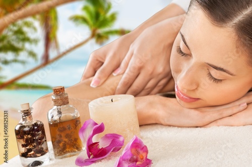 Beauty and relaxation concept - beautiful young woman on massage at spa over tropical beach background.