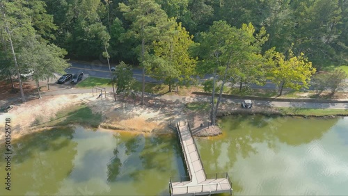 aerial footage of a silky green lake along a street with cars driving surrounded by lush green trees and grass at Huddleston Pond Park in Peachtree City Georgia USA photo