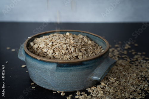 Side view of handmade ceramic bowl of organic oats on dark moody background with concrete wall.