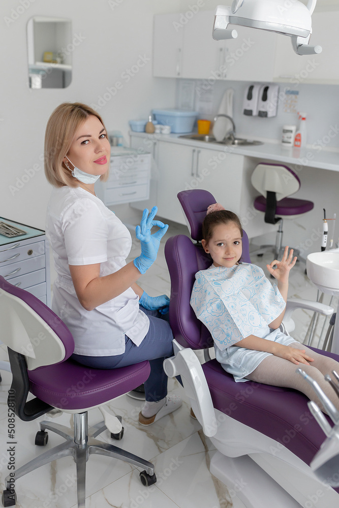 Dental clinic visit. Young positive woman dentist and small girl patient in dentist office Dental clinic visit. Young positive woman dentist and small girl patient in dentist office