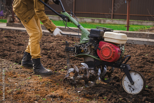 Wallpaper Mural Farmer cultivates the ground soil in the garden using a motor cultivator or tiller tractor. Modern farming and technology agriculture.  Torontodigital.ca