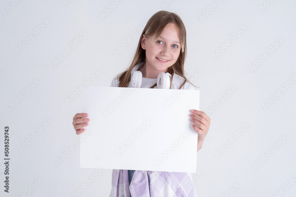 Portrait of a stylish long-haired blue-eyed teen girl with white horizontal A3 paper in her hands on a white background. Portrait of a stylish long-haired blue-eyed teen girl with white horizontal A3 paper in her hands on a white background.