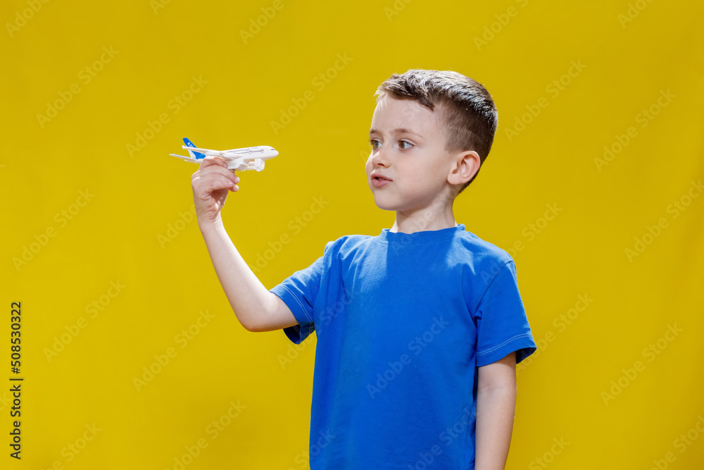 Little boy in a blue T-shirt holds a toy white plane and plays on a yellow background. Copy space. Travel concept Little boy in a blue T-shirt holds a toy white plane and plays on a yellow background. Copy space. Travel concept