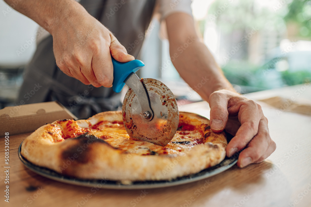 Hand of kitchen chef cutting pizza with a pizza cutter