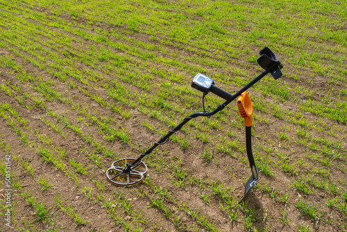Modern metal detector. Sensor for searching for metal underground. Metal detector and shovel without anyone. Treasure search equipment on ground with grass. Treasure hunting equipment