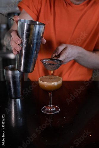 Barman is making cocktail at night club. stylish young man mixing a cocktail in a dark loft cafe. alcohol drink in modern bar. male bartender