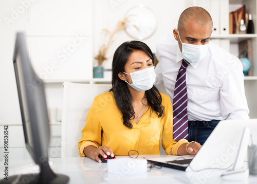 Director in protective medical mask gives instructions to secretary in office