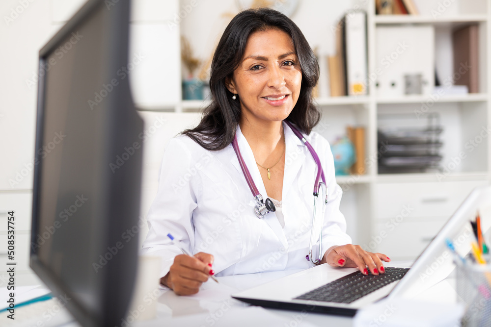 Portrait of smiling Colombian woman physician consulting patient in medical office - obrazy, fototapety, plakaty 