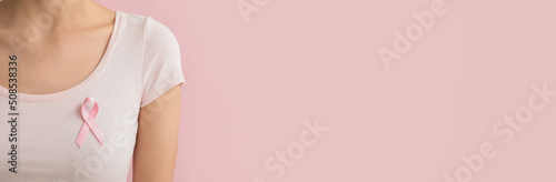 Woman with pink ribbon on color background with space for text, closeup. Breast cancer awareness concept