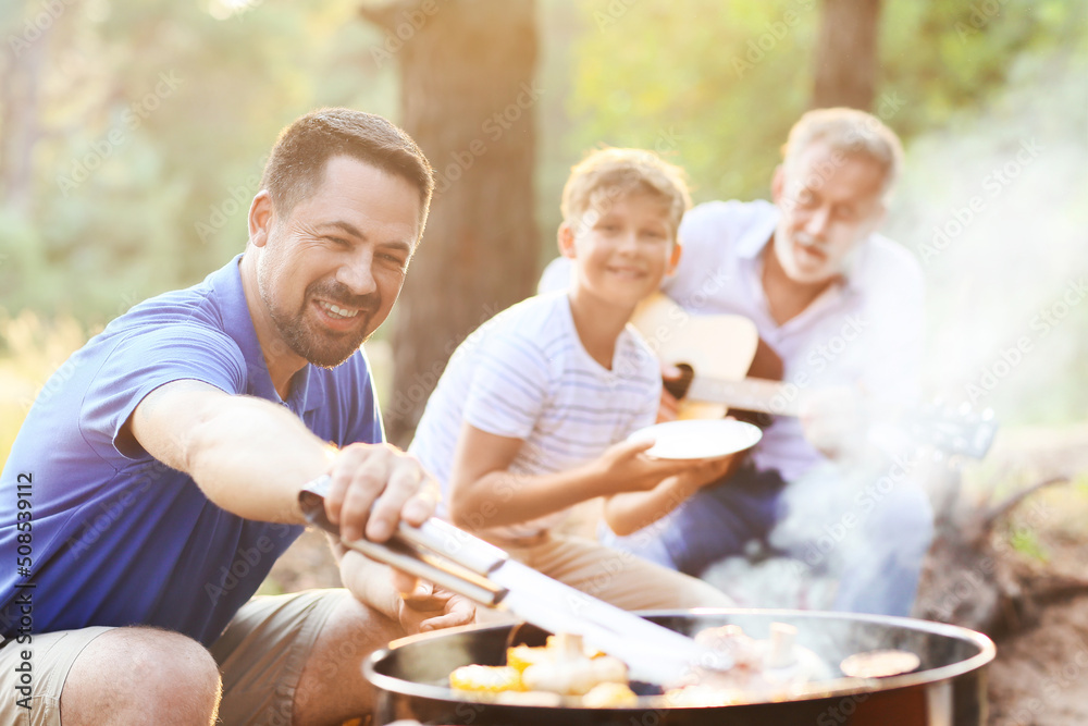 Handsome man cooking food on grill with his family at barbecue party Handsome man cooking food on grill with his family at barbecue party