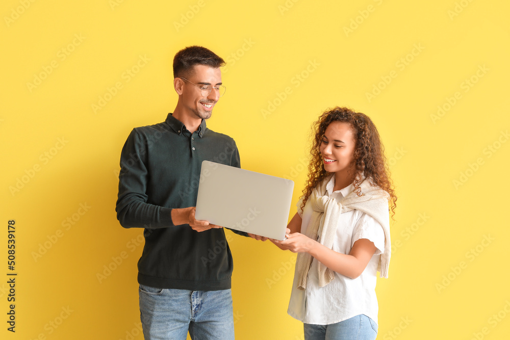 Young couple using laptop on yellow background Young couple using laptop on yellow background